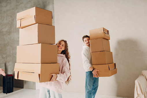 Happy young family couple man and woman carry cardboard boxes to new real estate apartment. Moving and delivery concept.