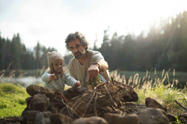 Dad and kid preparing campfire. Family camping at lake. copy space