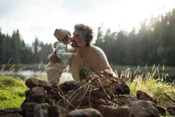 istock Dad and kid preparing campfire. Family camping at lake. copy space 1829353407