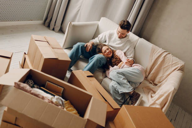 Happy young family couple man and woman relaxing after moving cardboard boxes to new estate home apartment stock photo