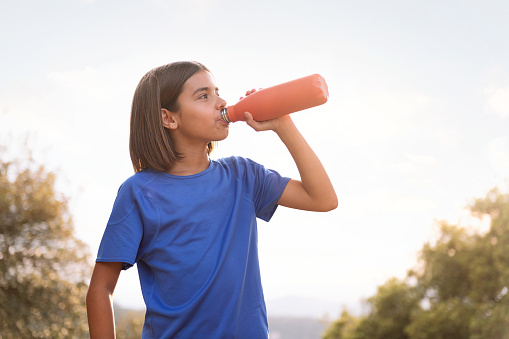 girl drinking water during her training, concept of sport in nature for children and healthy lifestyle