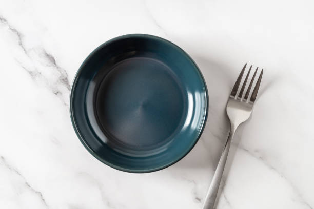 istock Dark blue ramekin and fork over marble tabletop. Empty clean ceramic bowl for food design mockup. Modern porcelain crockery and tableware concept. Dinnerware. High key image. 1829458547