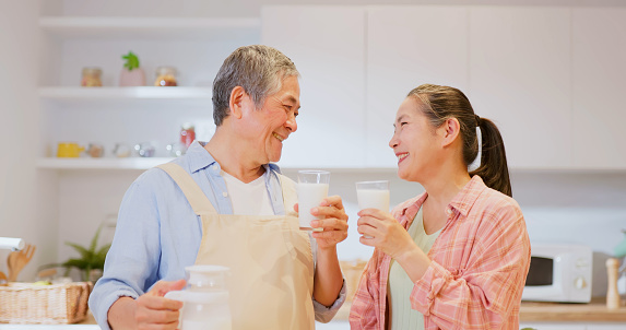 Close up view of asian elderly couple pour milk for each other in kitchen with smile and intimacy relationship