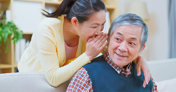 close up asian elderly couple embracing together look somewhere with smile and intimacy relationship sitting on sofa at home