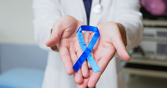 close up asian male doctor is holding blue ribbon on hands to disseminate colorectal cancer prevention and control