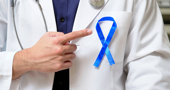 close up asian male doctor is pointing blue ribbon to disseminate colorectal cancer prevention and control