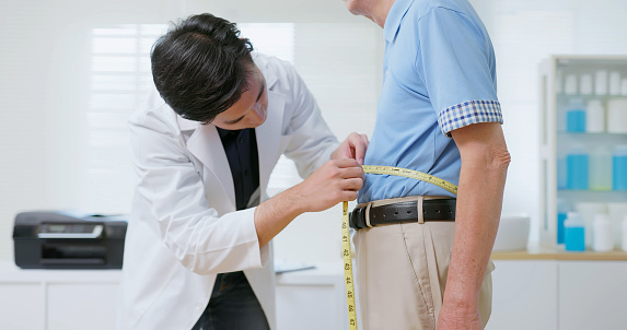 asian male nutritionist is measuring senior man waist with tape