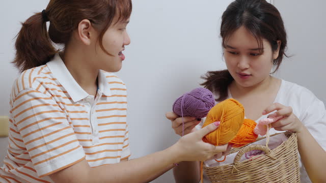 Two young Asian women learn to crochet by searching the internet using tablets. Hobbies in free time from studying.