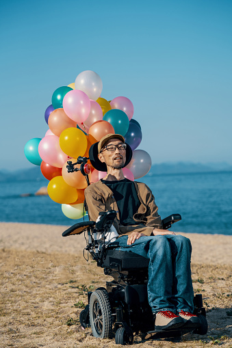Man with ALS in a wheelchair on the beach with a bunch of balloons
