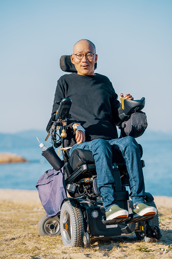Portrait of a man in a motorized wheelchair on the beach in Japan