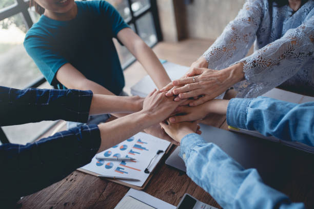 Young Asian business people shaking hands and working together as a team and having unity in working on new start-up project. Unity and Teamwork Concept. stock photo