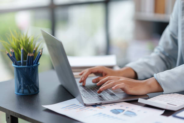 istock Close-up of a woman's hands sitting intently typing using laptop computer at the office fluently and several documents on the table. 1829695356