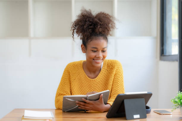 istock Woman student using tablet and holding book preparing for online class. 1829695469