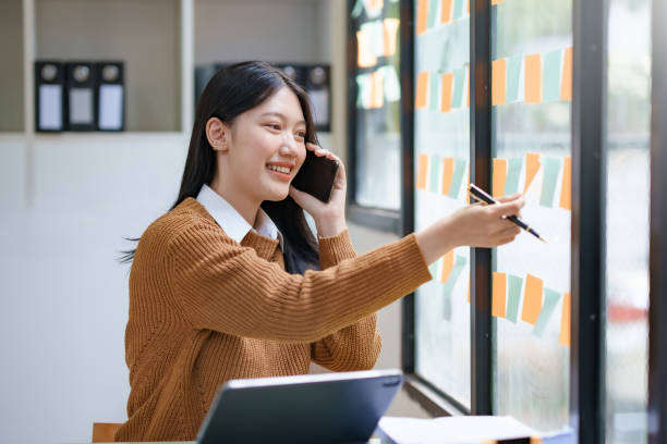 istock Asian businesswoman talking on the phone with clients while working and taking notes on a busy but happy working day in the office. 1829711455