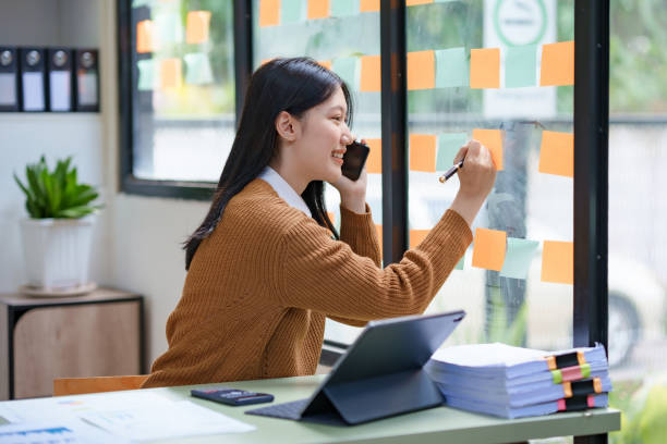 istock Asian businesswoman talking on the phone with clients while working and taking notes on a busy but happy working day in the office. 1829711467