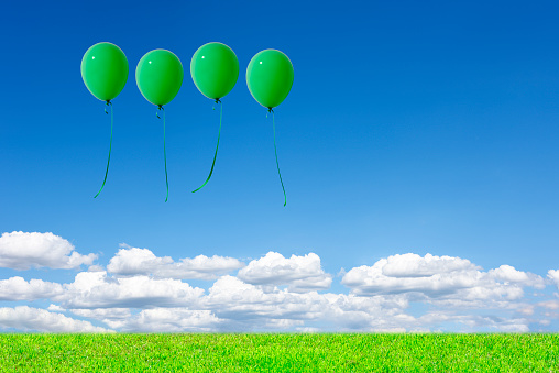 Four green balloons floating in the blue sky over the green hill with copy space.