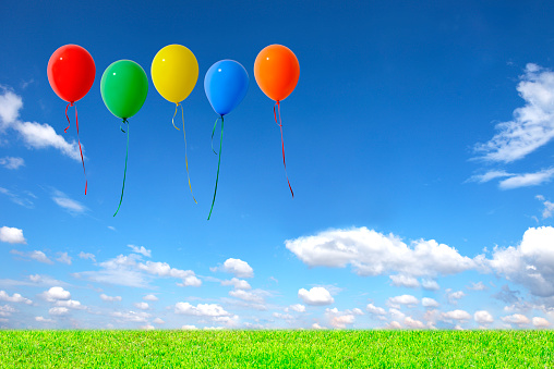 Five multicolored balloons floating in the blue sky over the green hill with copy space.