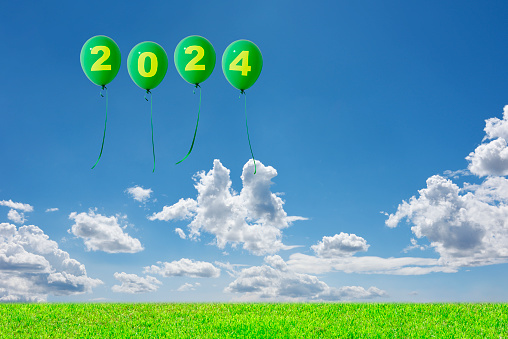 Four 2024 green balloons floating in the blue sky over the green hill with copy space.