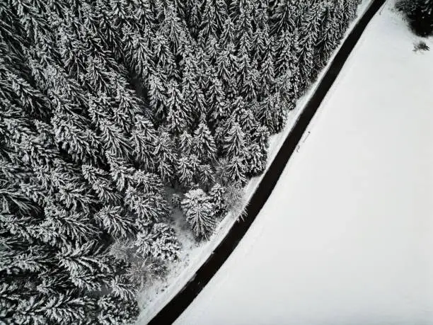 Empty winter road in snow covered forest, top down aerial drone photo, Black Forest, Baiersbronn, Germany