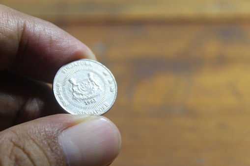 Close-up of left hand holding a euro coin with a table background