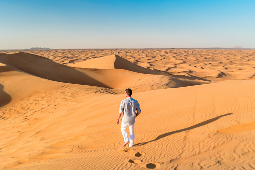 Dubai desert dunes, young men walking at the dunes of Dubai during a desert safari. man walking in the desert sand of Dubai