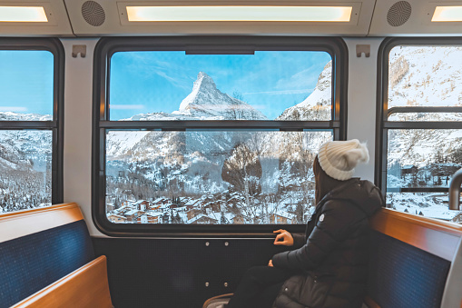 Happy Tourist woman looking out the window enjoying with the snow Matterhorn mountain while sitting in the train, Zermatt in Switzerland.