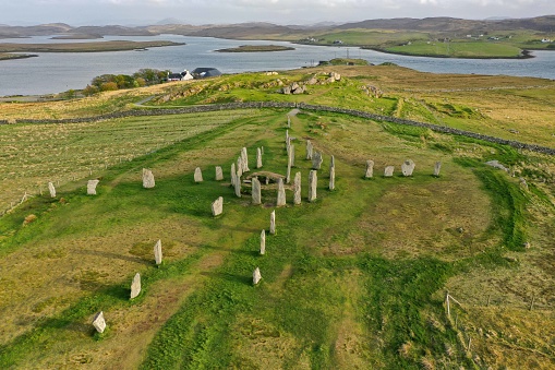 Sunset aerial drone view of the iconic Callanish Stones on the Isle of Lewis, in the Outer Hebrides of Scotland.  The ancient coastal standing stones date back 5,000 years. They remain a mystery, but were perhaps an astronomical observatory. A later added chambered tomb is seen within the main stone circle.