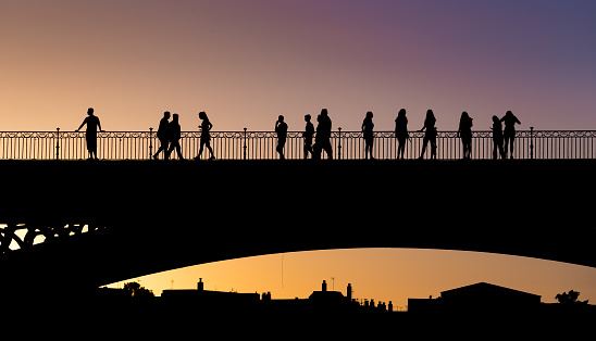 Silhouettes of people crossing the Triana bridge in Seville at sunset on a summer day