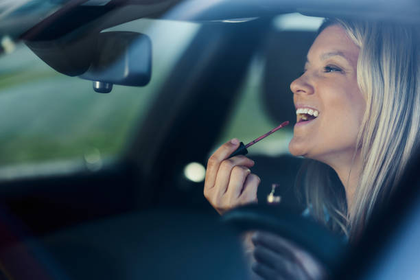 istock Happy woman applying lip gloss in a car. 1829899781