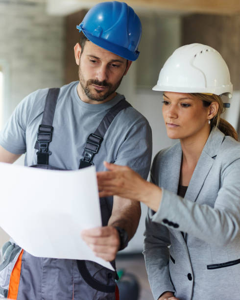 istock Female inspector and manual worker reading plans at renovating home. 1829909036