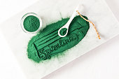 A beautiful inscription made of sprinkled green spirulina powder and a ceramic spoon filled with it. white background. Natural food supplements.