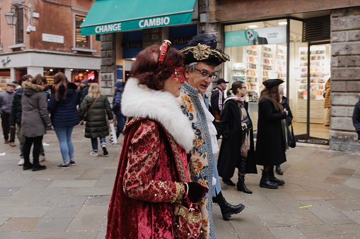 Venice, Italy - February 16 2023: Fully masked couple walking down a stone paved street in Venice, town full of tourists at the time of traditional Carnival, day in winter