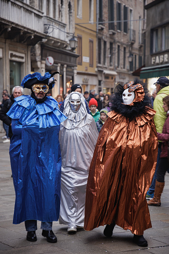 Venice, Italy - February 16 2023: Three fully masked people walking down a stone paved street in Venice at the time of traditional Carnival, day in winter