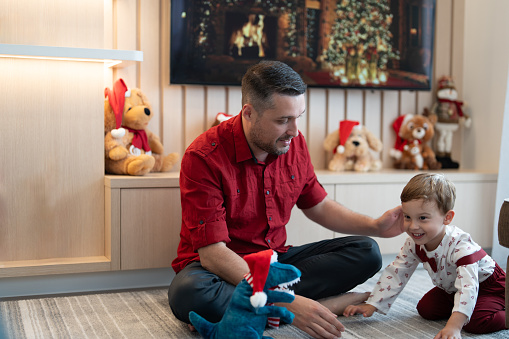 Father with kid playing with a dinosaur toy at home, celebrating Christmas.