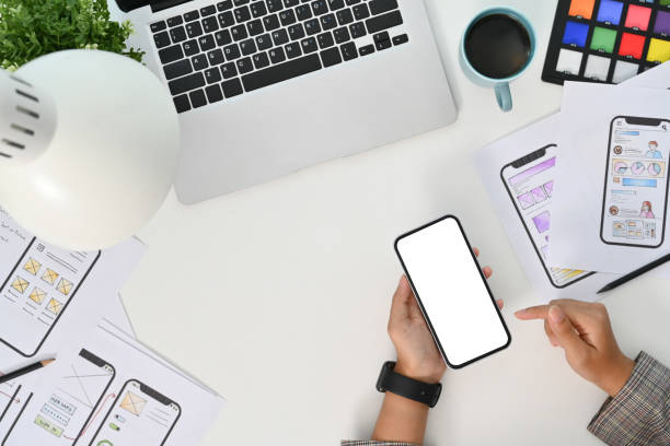 istock Young creative woman using mobile phone at desk with paper sketches for mobile interface 1829960673