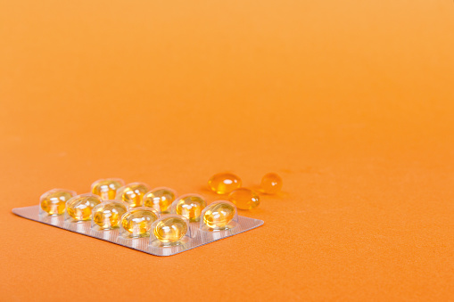 Blister package with fish oil capsules on color background. Medicine pills on a light background. Medicines and prescription pills flat lay background. Yellow medical tablets in blister.