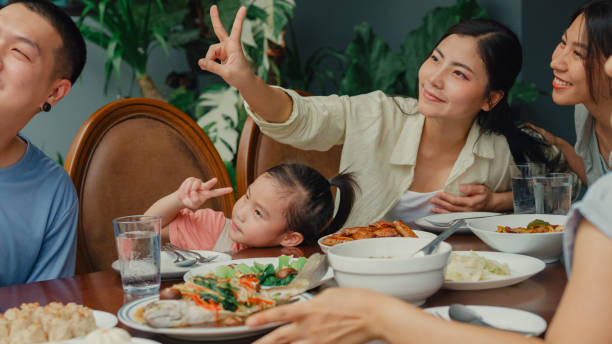 istock Young Asian family using mobile phone taking selfie and having fun sitting at dining table at backyard outside home. Multi-generation family enjoying spending together. 1830013971
