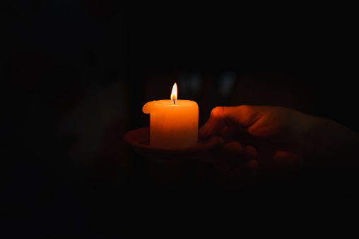 Religious concept.Boy holds in a hand a burning candle against black background.