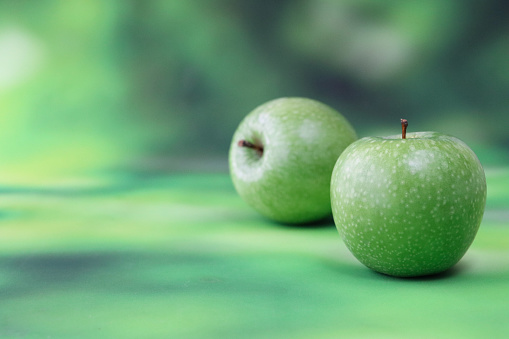 Stock photo showing close-up view of two, green Granny Smith applestwo with shiny, speckled skin against a mottled green background.
