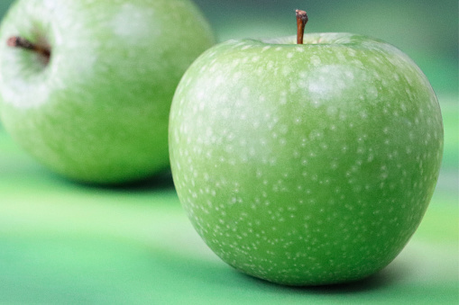 Stock photo showing close-up view of two, green Granny Smith applestwo with shiny, speckled skin against a mottled green background.