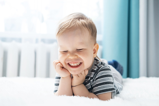 Portrait of a cheerful laughing little boy lying on a bed