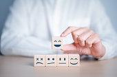 Hand chooses smiley happy face on wooden cube from normal and sad emotion on others. World Mental Health Day, Feedback rating, Customer service review. Think positive and satisfaction survey concept.