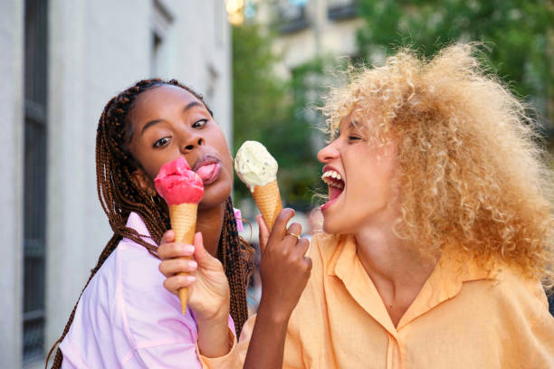 Two multiracial happy friends with ice creams making funny faces in summer.