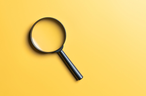 Close up of a magnifying glass on a yellow background. Science research concept. Top view. Flat lay. Copy space. Finding, searching for ideas, search for information, find out. Magnifier finds answer.