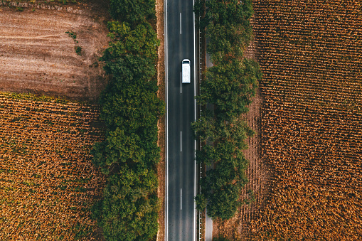 White commercial van vehicle driving along the highway road through countryside landscape, aerial shot from drone pov, directly above