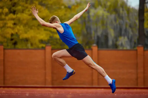 Athlete's controlled sprint before liftoff. Side view full length portrait of professional sportsman fast running on sport field. Concept of kinds of sport, championship, motivation, energy.