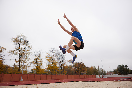 Fitness, athletics high jump by man at a stadium for training, energy and cardio against sky background. Jumping, athlete and male outdoors for performance, endurance and competition on mock up