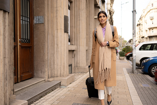 Happy female entrepreneur pulling her luggage while going on a business trip in the city.