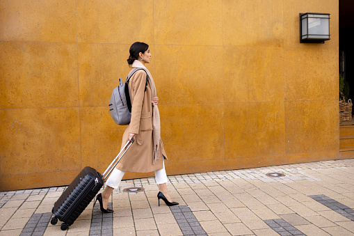 Side view of happy businesswoman walking with a suitcase on the street. Copy space.