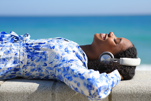 Happy black woman lying listening music on the beach